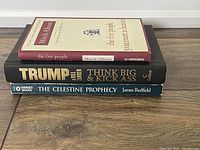Stack of three books: The Five People You Meet in Heaven hardcover on top, Trump hardcover in middle, Celestine Prophecy softcover on bottom