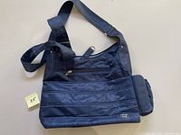 Blue LUG tote bag front and side view showing quilted pattern, front zippered pocket, side expandable pocket, and adjustable strap.