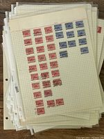 Stack of plastic sleeves containing sheets of red and blue Canadian stamps, mostly postmarked, on graph paper.