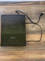 Top view of the black Master Chef induction cooktop burner with power cord shown on wood floor surface.