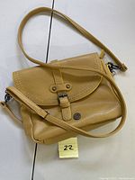 Front and side view of mustard-colored pebble leather crossbody handbag with flap and buckle detailing.