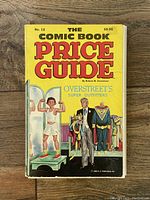 Front cover of the Overstreet Comic Book Price Guide #12 from 1982 on wood surface, showing bold colorful title and illustration of boy and man with costumes.