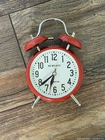 Front view of red Newgate alarm clock showing analog face and twin bells.