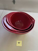 Side view of three nested red mixing bowls showing size differences and pouring spouts.