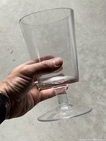 Hand holding a single clear glass vase showing its shape and size relative to hand