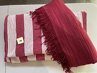 Folded king size duvet cover with vertical wine and white stripes alongside a folded maroon throw with fringed edges laying on top.