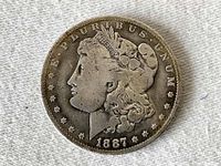 Obverse side of the 1887 Morgan silver dollar showing Lady Liberty's profile with the inscription E PLURIBUS UNUM and date 1887 below.