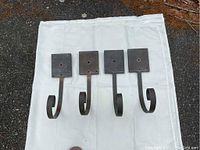 Four copper wall plant hangers laid out on white fabric, front view showing square wall plates with wiring holes and curved hooks.