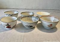 Front view of all six porcelain cups showing varied hand-painted designs and footed bases.