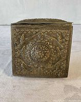 Front view of the antique metal pouch/box showing embossed floral and circular geometric designs.