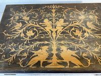 Top view of the closed wooden vanity box showing detailed engravings of griffins, cupids, and floral patterns in gold on a dark wood surface.