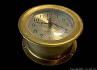 Close up angle of brass case ship's clock showing the clock face, hands, and markings