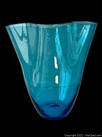 Front view of the blue ruffled glass vase against a black background showing its shape and top ruffle detail.