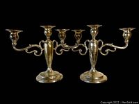 Full front view of the pair of sterling silver candelabra on black background, showing the overall design and shape.