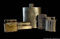 Photo of a 3 oz pewter hammered flask with four vintage lighters, showing detailed surface and condition in low light.