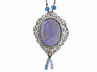 Front view of the vintage pendant necklace showing the periwinkle oval agate stone framed in detailed metal filigree with bead tassels at bottom and two periwinkle beads at top near chain attachment.