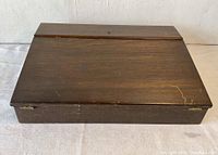 Closed wooden travel writing desk box from an angled front view showing wood grain and slight scratches.