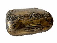 Side view of the antique sterling silver soap box showing the hinged design and detailed floral scrollwork with worn goldish tone.