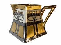 Side angle view of small square pitcher showing gold gilding on handle and spout, floral decorations on white background, and metallic gold and silver panels on sides.