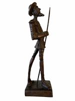 Side view of the wood Don Quixote statue showing the figure holding a lance on a wood base.