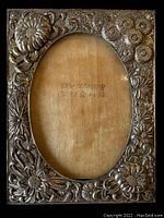 Front view showing detailed embossed floral design on metal picture frame with oval opening.