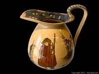 Front side view showing Night Watcher figure and village scene on pitcher body with curved handle and flared spout