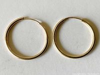 Pair of 14K gold hoop earrings laid flat showing circular shape and latch closure.