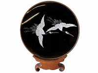 Front view of the Japanese cloisonné dish showing two white cranes in flight on a black background, placed on a wooden stand.