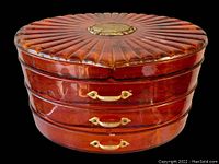 Front view of the closed jewelry box showing three drawers with gold-tone handles and sunburst lid pattern with central medallion