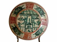 Front view of the ceramic dish showing traditional painted design with animals and architectural motifs in green and red.
