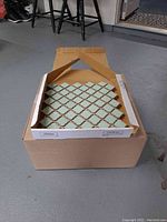 Photo of multiple ceramic mosaic tile sheets in an open cardboard box, showing the pattern and color of the tiles.