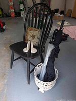 Full view of black wooden spindle back chair with white cast iron bookends resting on seat and a decorative tin wall hanging behind. White wicker basket holding two umbrellas placed next to chair.