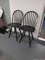 Two black wooden spindle back swivel chairs side by side against a white wall, showing overall condition and style.