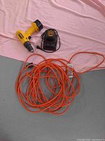 DeWalt cordless drill model DW926, black charger, orange outdoor extension cord laid out on floor with pink cloth background