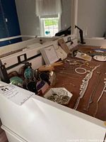 Wide angle photo showing jewelry and sunglasses on brown fabric, including necklaces, bracelets, rings, earrings and multiple pairs of sunglasses.