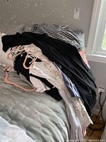 Pile of assorted clothing items in black, white, pink, and blue colors on a bed.
