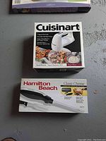 Boxed Cuisinart 7 speed hand mixer and Hamilton Beach Electric Carver boxes shown on a surface.
