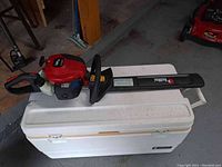 RedMax CHT220 hedge trimmer laying on a white cooler, showing full side and top views with the RedMax branding visible on blade protection and trimmer body.