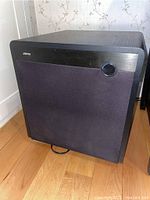 Front view of Jamo subwoofer speaker with black fabric grille and metallic ring accent on grille.