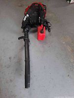 Blower with harness and tube plus red gas can arranged on concrete floor