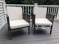 Two wooden patio chairs with seat and back cushions placed on a wooden deck.