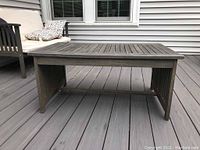Front view of wooden outdoor patio coffee table on a gray deck with surrounding patio seating.