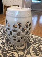 Side view of white ceramic plant stand showing intricate cut-out floral design and raised dots near the top.
