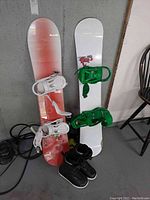 Two snowboards, one red with white bindings and one white with green bindings, with black boots in front.