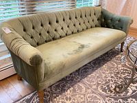 Front view of green velvet sofa showing tufted back and rolled arms, slight discoloration on seating area.