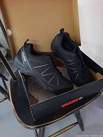 Pair of black Wolverine steel toe hiking shoes inside box, showing left and right shoe with mesh and synthetic upper, lace closure, and Wolverine branding on side and tongue.