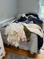 Photo of BED with pile of folded and unfolded sweaters, sweatshirts, and jeans mostly in casual styles, sizes extra small and small.