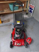 Front view of mower on concrete floor, grass bag attached, fuel can at front wheel
