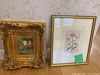 Photo showing both framed artworks side by side against floral wallpaper. Left is the ornate gold frame with oil painting of children playing. Right is framed flower print with white mat and gold frame.