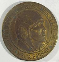 Obverse of brass coin showing Amelia Earhart portrait with text around edge.